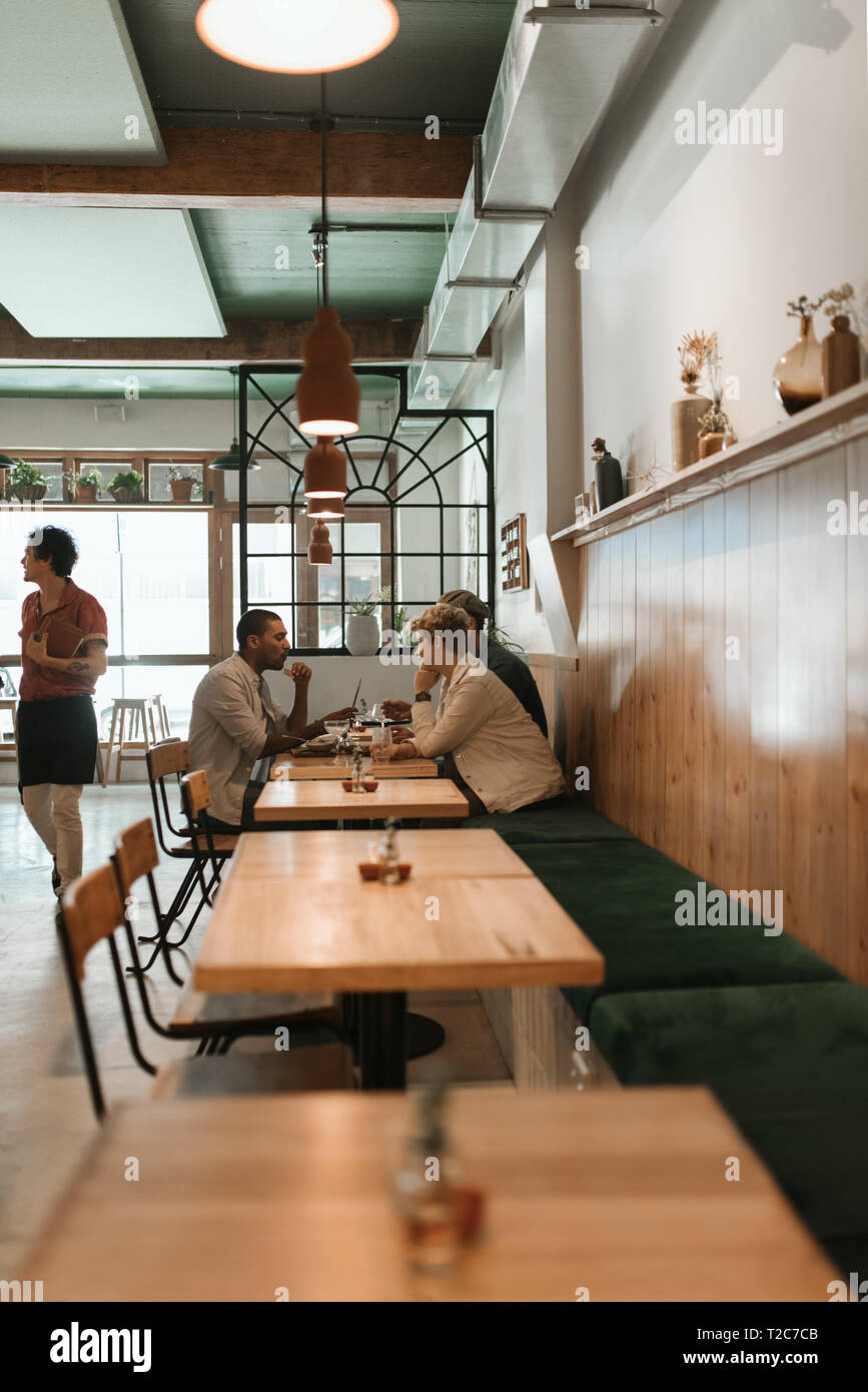 Lächelnd Gruppe von verschiedenen jungen Freunde reden über Mittagessen und Getränke zusammen an einem Tisch in einem schicken Restaurant Stockfoto