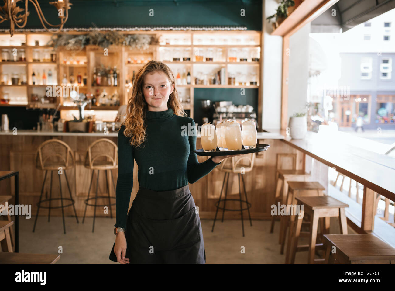 Porträt einer freundlichen jungen Kellnerin in einem Bistro mit einem Fach an Cocktails Stockfoto