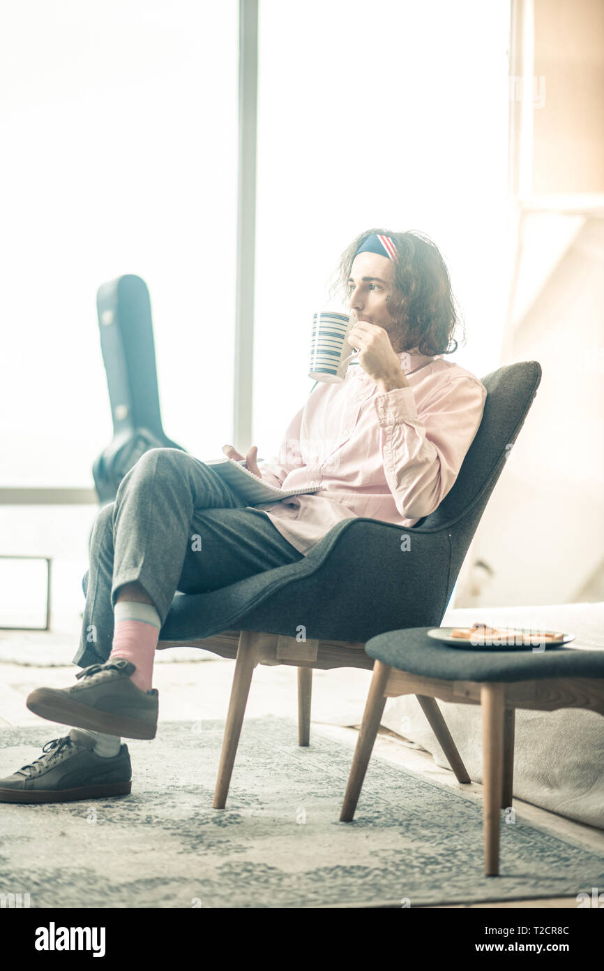 Nachdenklich langhaarigen Mann in stilvollem Outfit Tee trinken, beim Stillstehen Stockfoto