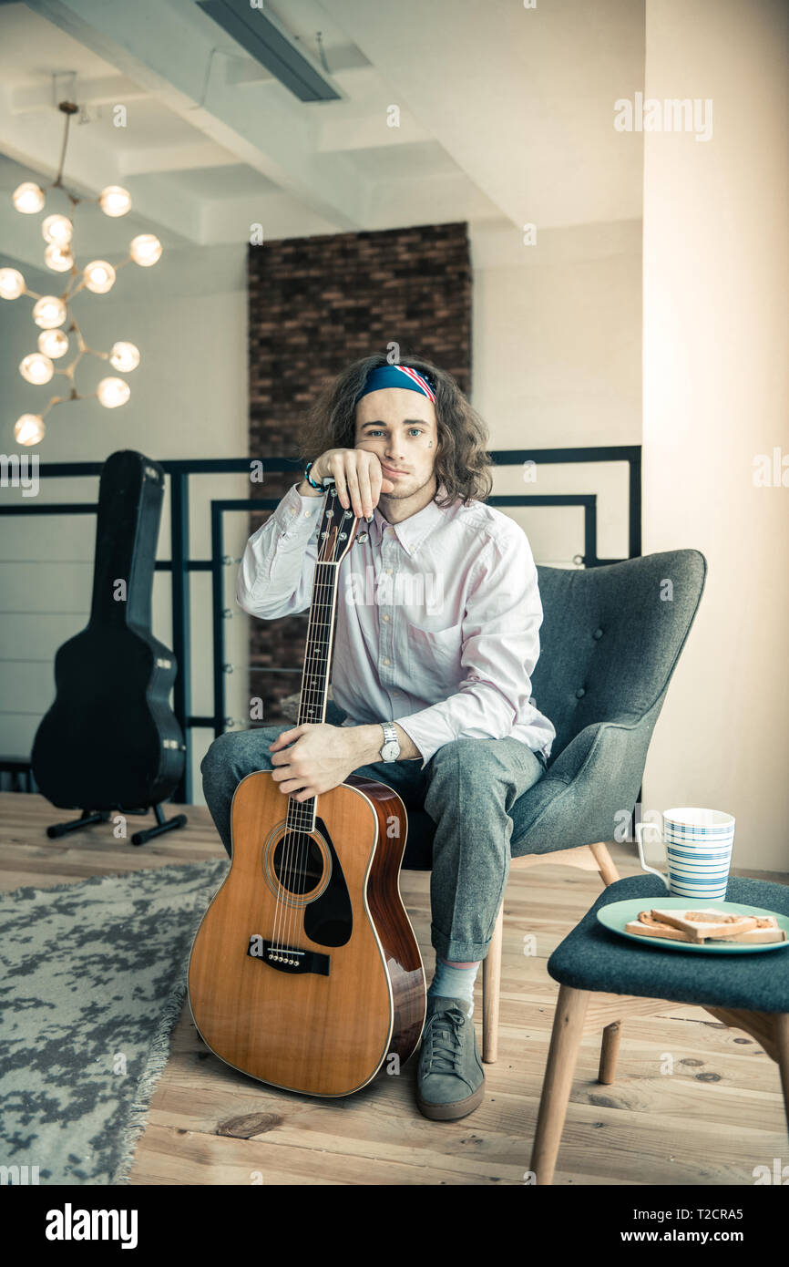 Müde umgekippt Kerl mit bunten Bandana lehnte sich auf seiner Gitarre Stockfoto