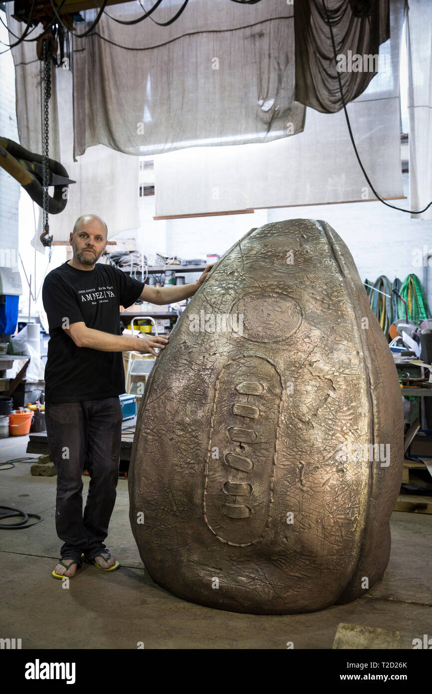 Bildhauer Gavin Turk mit seinem rugby ball Skulptur 'Geburt der Ei Ball" auf seiner Bronze geschmiedet Bühne der Schöpfung für Rugby School, dem Geburtsort des s Stockfoto