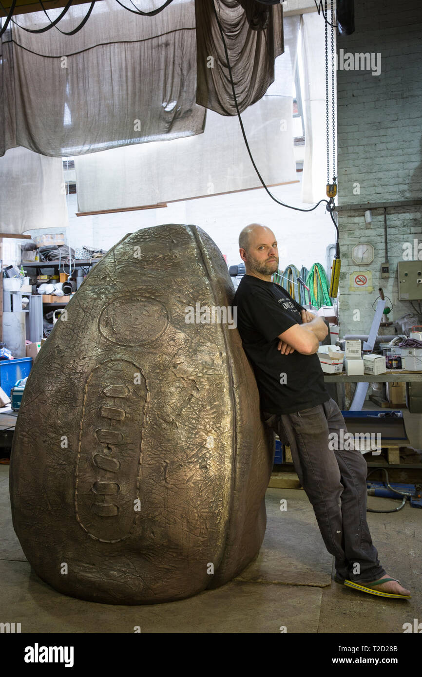 Bildhauer Gavin Turk mit seinem rugby ball Skulptur 'Geburt der Ei Ball" auf seiner Bronze geschmiedet Bühne der Schöpfung für Rugby School, dem Geburtsort des s Stockfoto