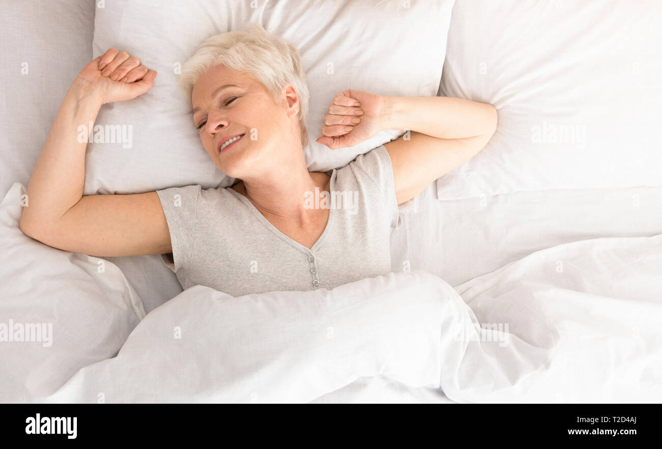 Gut schlafen. Gerne ältere Frau Stretching im Bett, Erwachen am Morgen Zeit, Ansicht von oben, Panorama mit leeren Raum Stockfoto