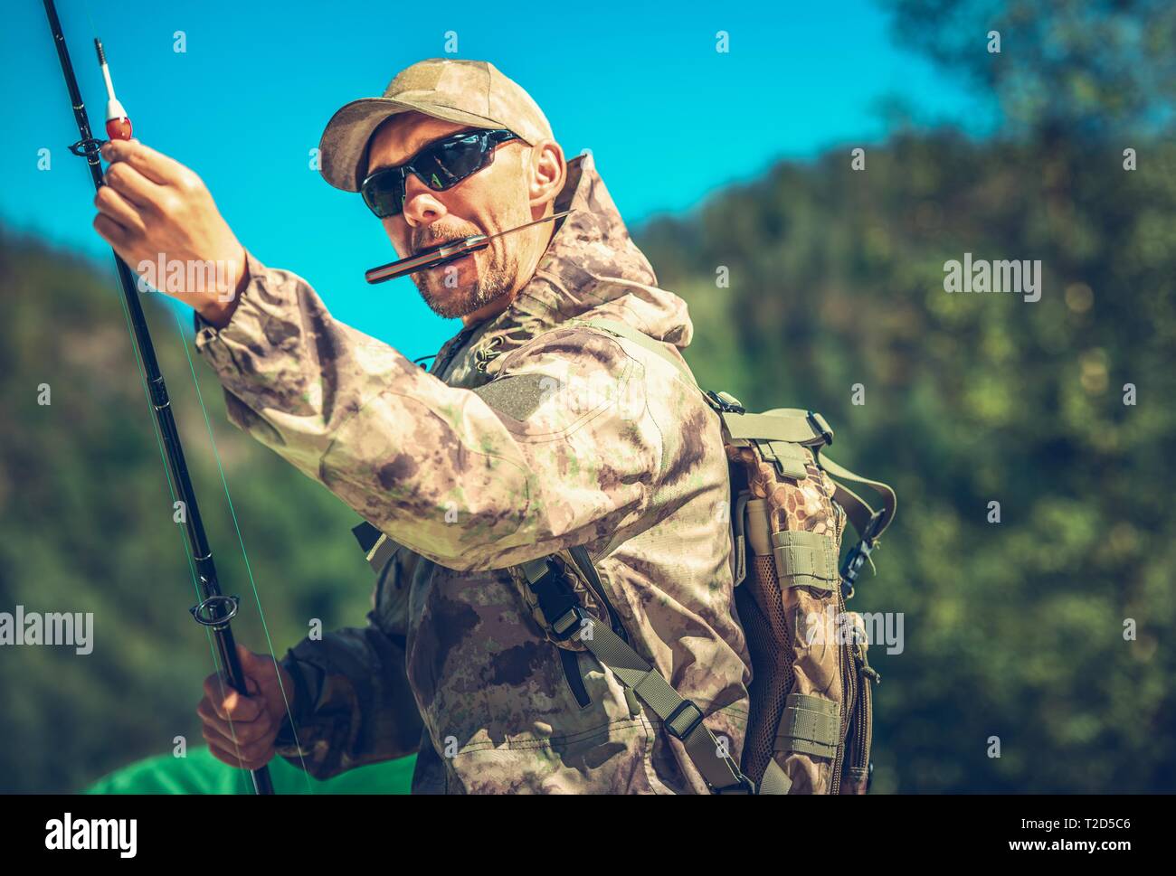 Kaukasische Fischer in seinem 30s mit Messer im Mund die Vorbereitung für eine Fliege Fischen. Stockfoto