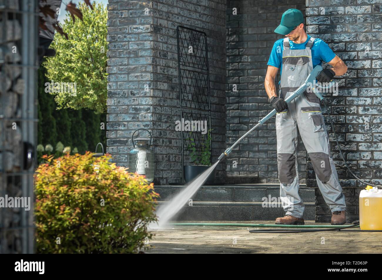 Auffahrt Waschen unter Druck. Kaukasische Arbeiter Reinigung Bereich vor dem Haus. Stockfoto