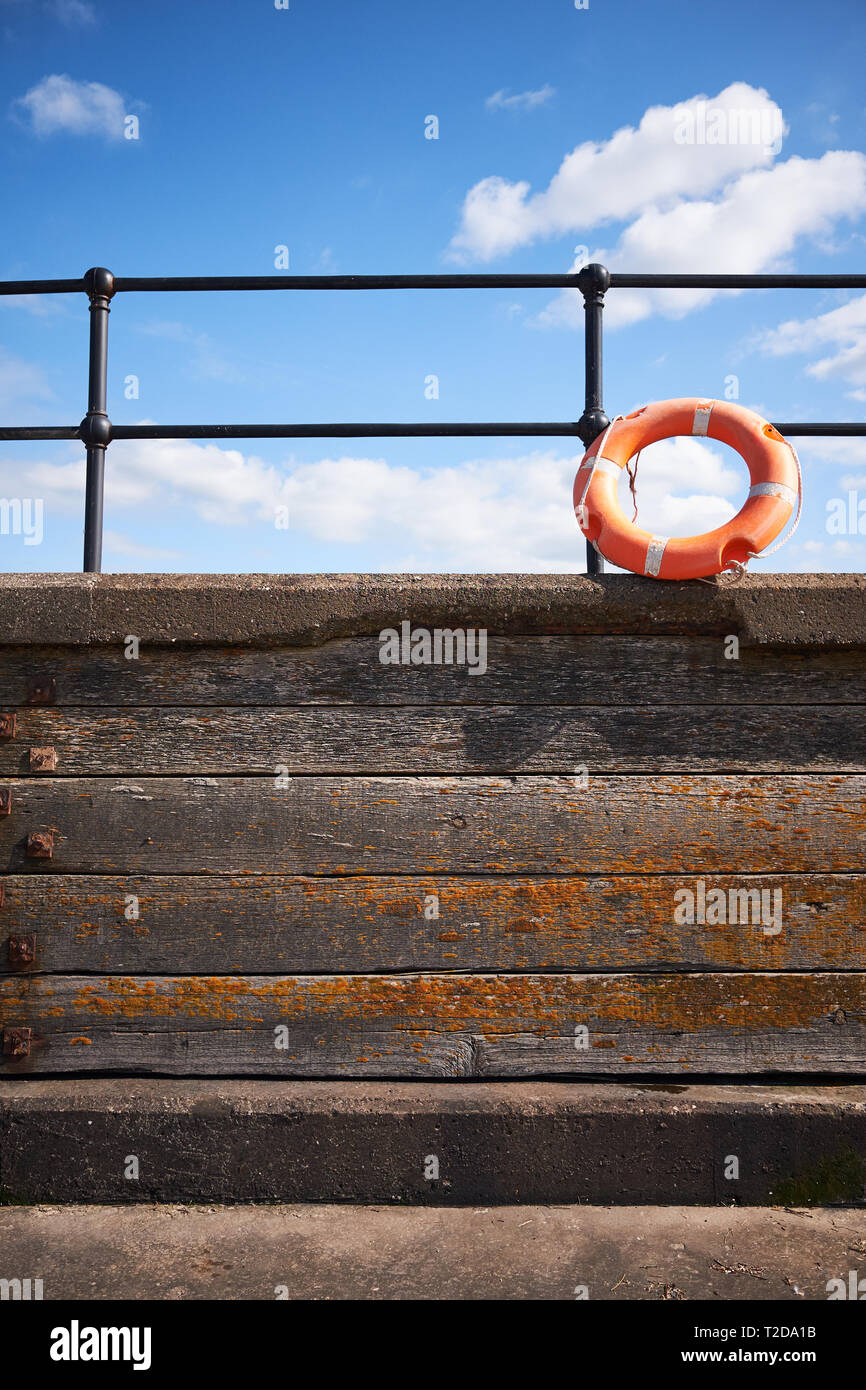 Während der Sommersonne ruht auf einer Strandpromenade in Liverpool eine orangefarbene Lebensbouy an einer Handschiene. Stockfoto