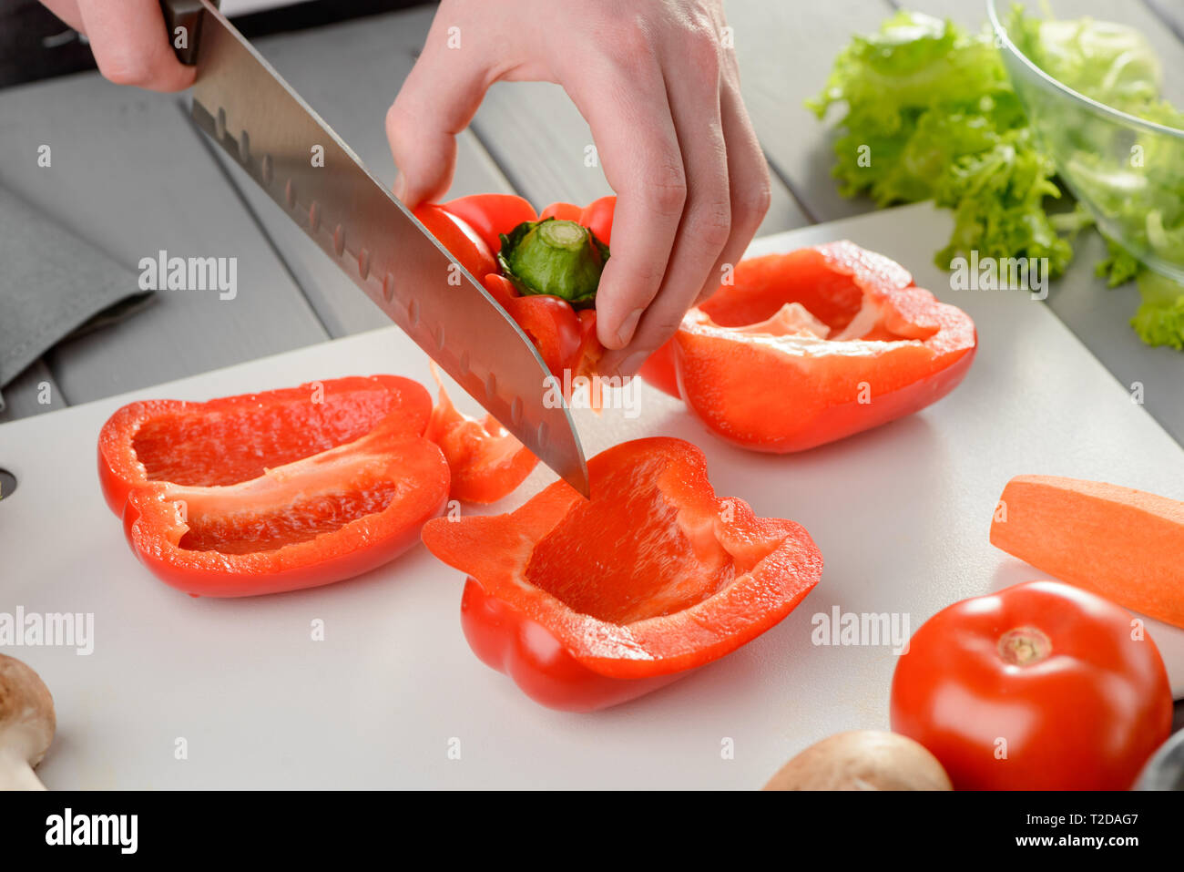 Mann eine Paprika im Quartal mit einem Santoku Messer. Kochen, Arten von Schneiden von Gemüse. Stockfoto