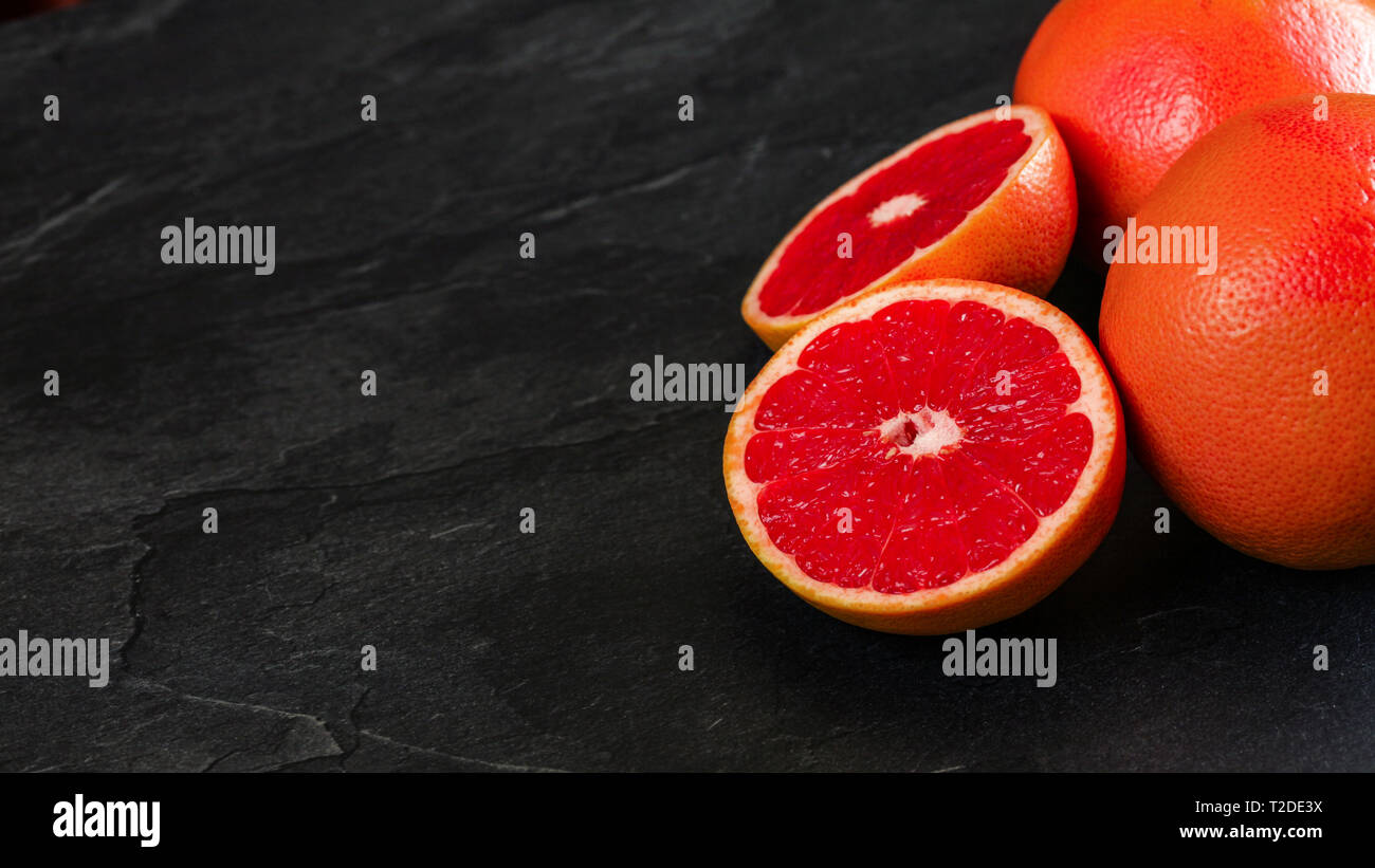 Rosa Grapefruits, einer Zitrusfrucht halbieren, auf schwarzem Schiefer wie Vorstand, große Banner mit Platz für Text mit Links. Stockfoto