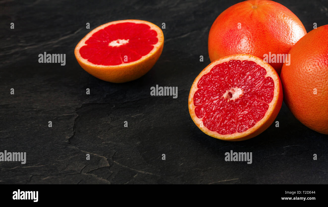 Rosa Grapefruits, einer Zitrusfrucht halbieren, auf schwarzem Schiefer wie Vorstand, Platz für Text links in die Ecke. Stockfoto