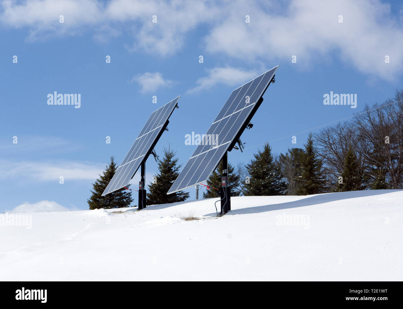 Freistehende Photovoltaik-Solarpaneele mit Stangenmontage auf einem Hügel in einer ländlichen Winterumgebung. Stockfoto