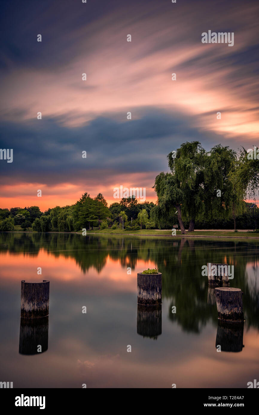 Lange Belichtung geschossen am Abend bei Sonnenuntergang an einem See in einem Park mit baumstümpfen im Vordergrund und schöne Reflexionen Stockfoto