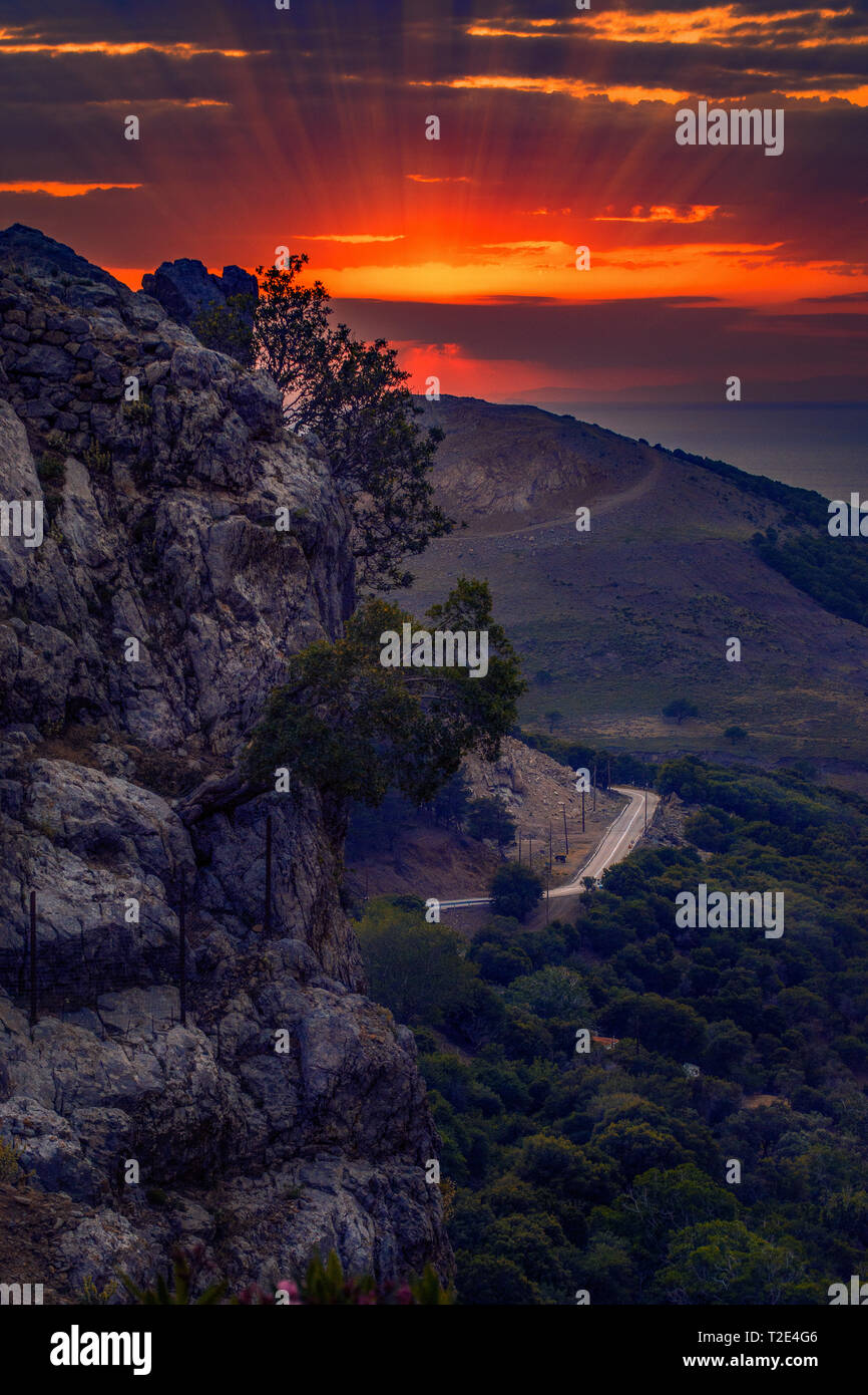 Lebendige Sonnenuntergang über den Bergen von Samothrake Insel in Griechenland mit einer Straße in den Hintergrund und die Klippen im Vordergrund. Stockfoto