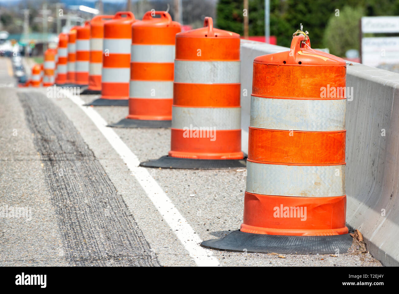 Horizontale Nahaufnahme von Orange und Weiß Gestreifte Verkehr Fässer an der Seite von einer Straße mit geringer Tiefenschärfe. Stockfoto