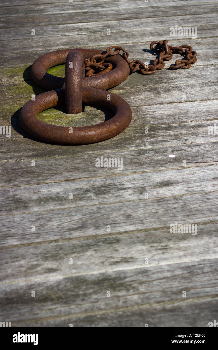 Low Angle Hochformat von zwei rostige verwitterte Liegeplatz Ringe mit kleiner Kette auf Holz Brett Belag Stockfoto