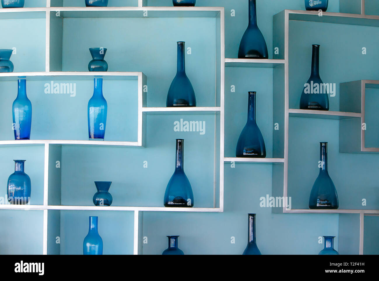 Retro Style Blau Glas Flaschen in einer schönen Anordnung in den Regalen zu einem hellblauen Wand befestigt. Stockfoto