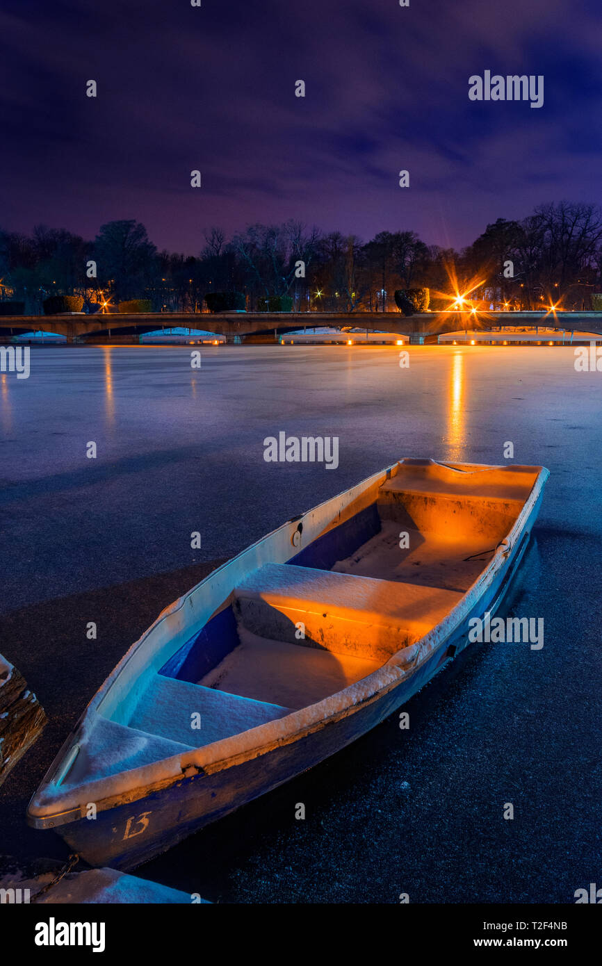 Gefrorenen See mit Boot im Winter geschossen während der Nacht in einem Park in Bukarest Rumänien mit einer Brücke im Hintergrund und Kunstlicht. Stockfoto