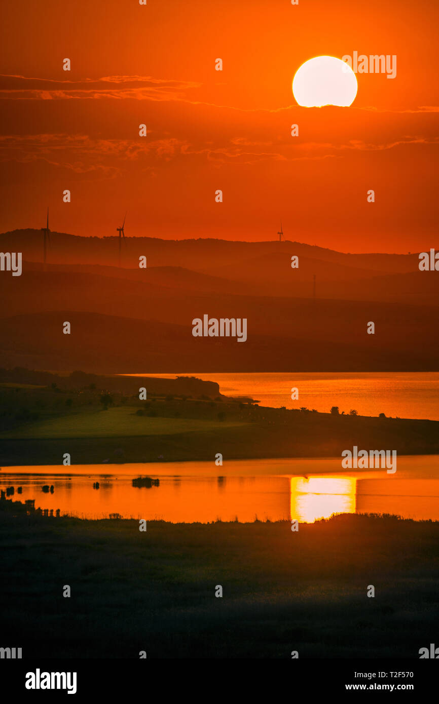 Äolische Windenergieanlagen auf Hügeln verwendet ökologische Ökostrom Schuß bei Sonnenuntergang mit einem See im Vordergrund und lebendige Farben zu produzieren platziert Stockfoto
