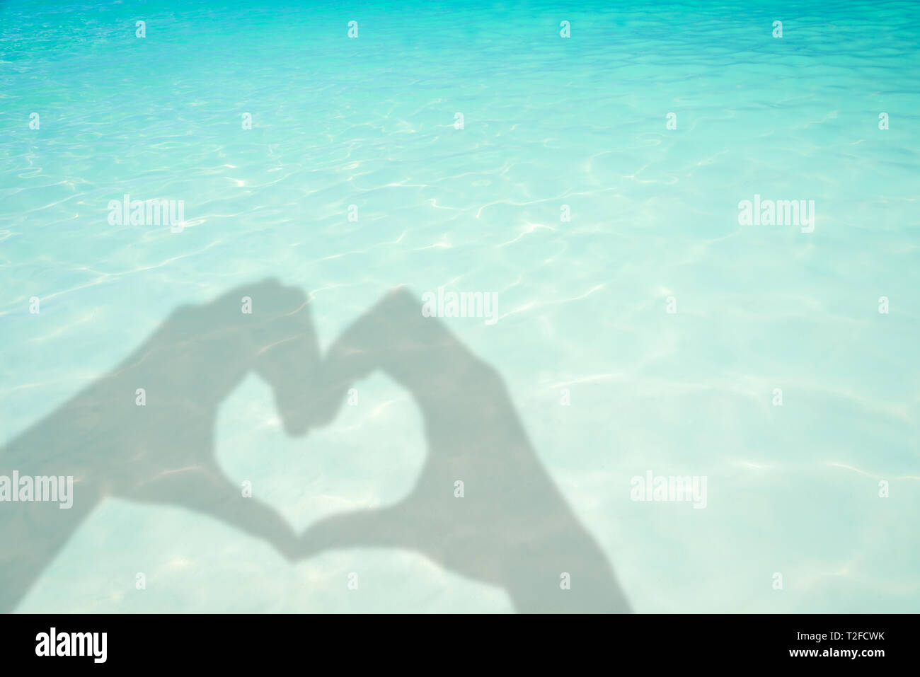 Schatten der Hände bilden ein Herz auf Türkis transluzent Wasser Meer Hintergrund Stockfoto
