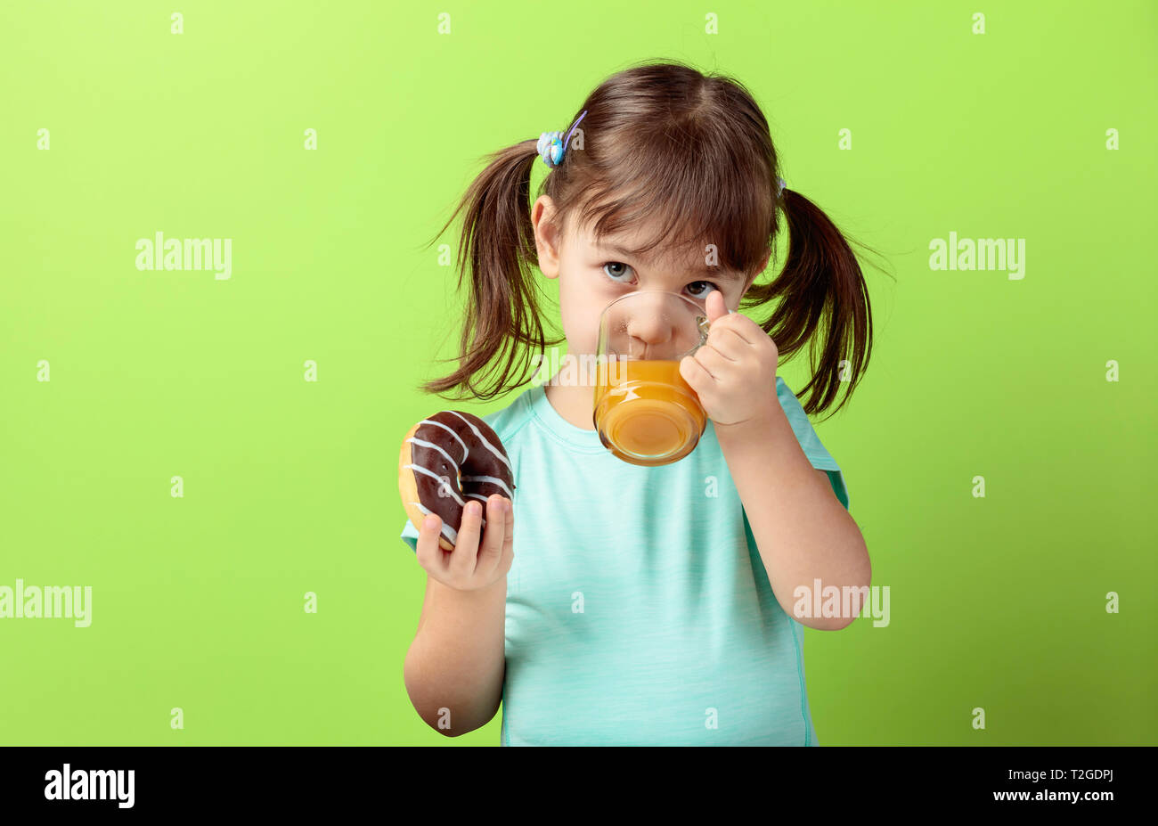 4-Jähriges Mädchen in einem Türkis t-shirt essen und trinken Saft. Das Haar des Mädchens in Schwänze gebunden ist. grünen Hintergrund. Stockfoto