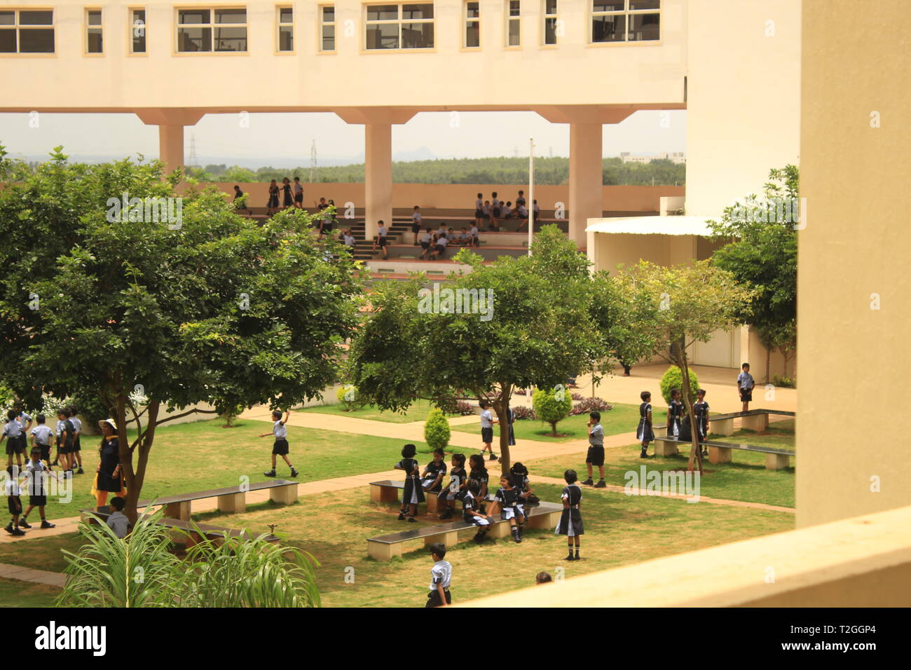 Kinder und Schüler in der Schule Garten mit Bäumen und eine Brücke, die Gebäude im Hintergrund in Excel P Schule in Mysore spielen Stockfoto