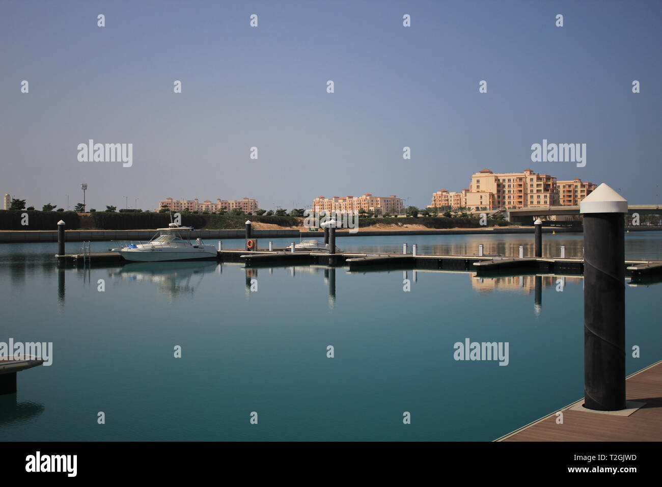Eine kleine Yatch bei kleinen Dock oder den Hafen in einer Bucht vom Meer mit ruhigem Wasser widerspiegelt mit Gebäuden weit entfernt. In KAEC. Stockfoto