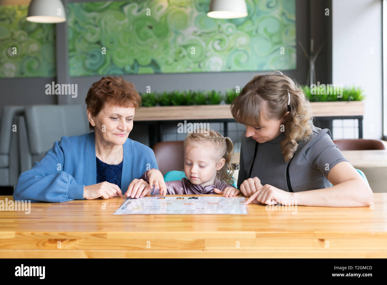 Weibliche Familie mit drei Generationen von Frauen Enkelin Mutter und Großmutter beobachten das Menü in einem Restaurant Stockfoto