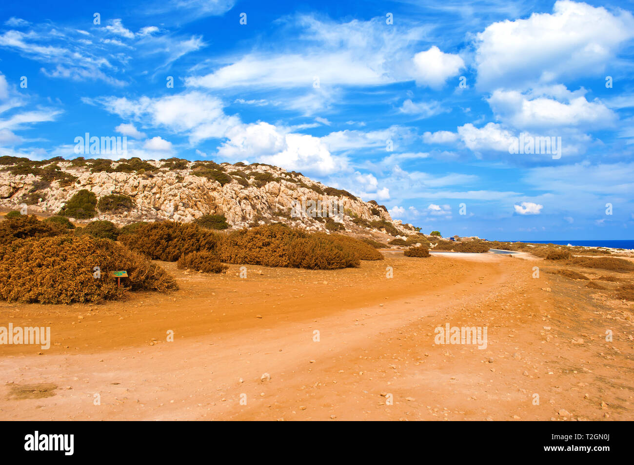 Bild von rauhem Kalkstein Küste in der Nähe von Kap Greco, Zypern. Cloudscape mit vielen weißen Wolken im Himmel, kargen orange sandigen Weg, Weite. Warm Stockfoto