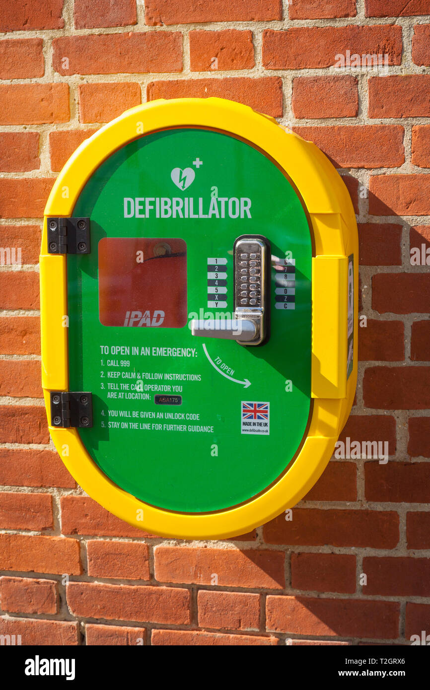 Leuchtend gelber und grüner, öffentlich zugänglicher Defibrillator (PAD) an einer Ziegelwand der Feuerwehr Henley-on-Thames Stockfoto