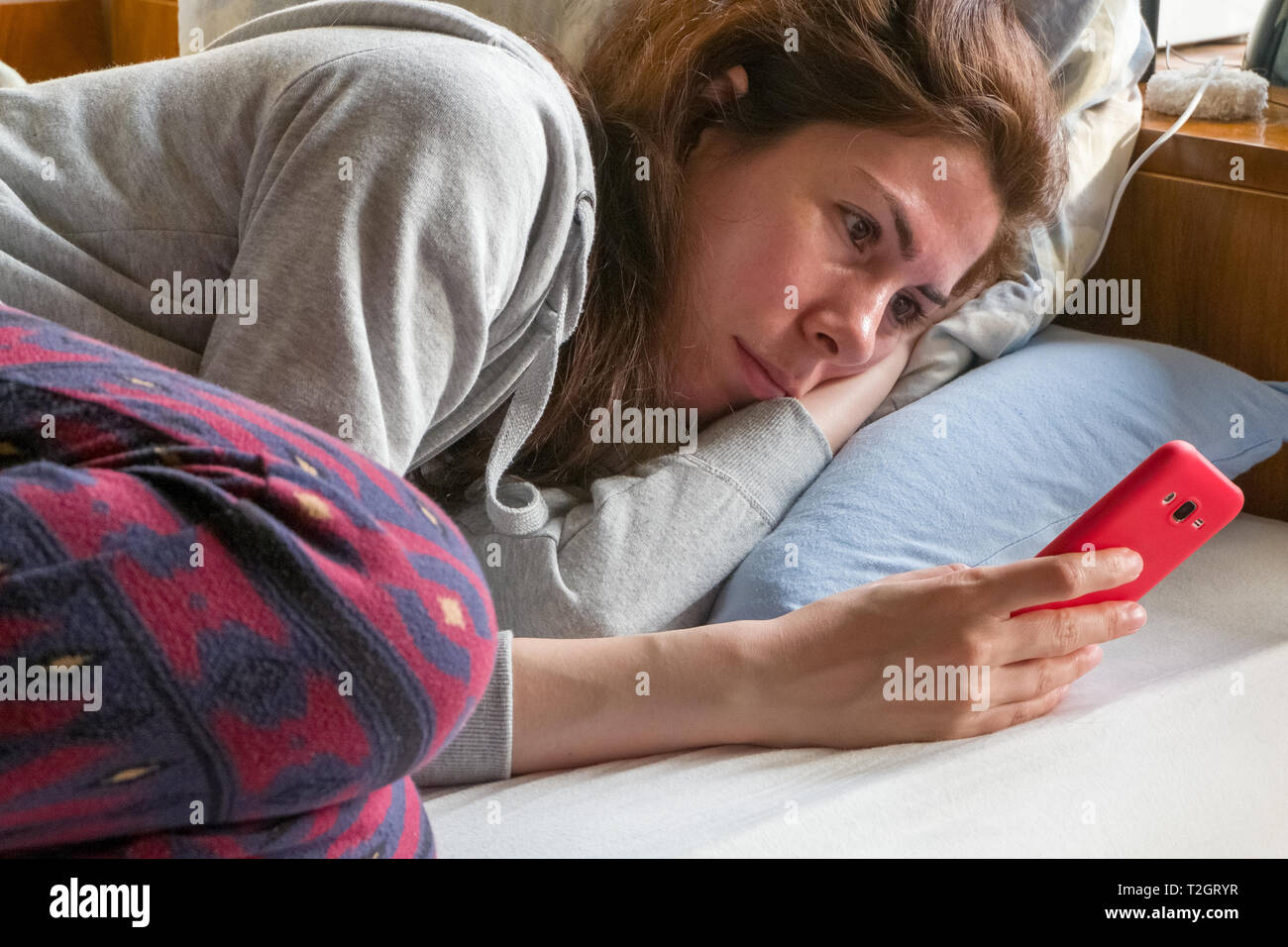 Junge Frau im Bett lag, entspannend und das Handy. Stockfoto