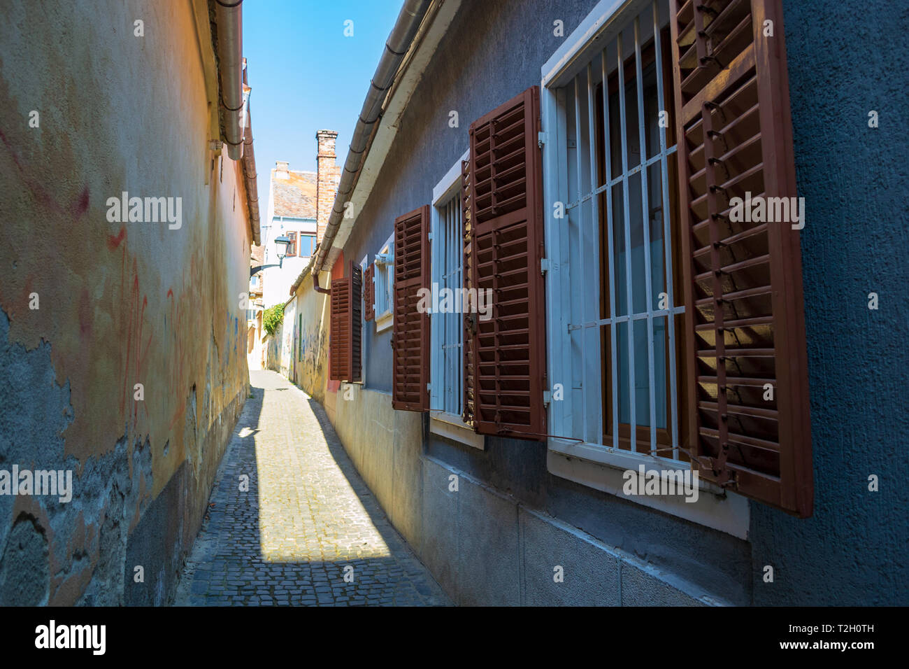 Fensterläden aus Holz, aus denen geschlossen weißes Fenster Balken auf einer schmalen Straße in Sibiu (Hermannstadt), Rumänien eröffnet. Geschrumpfte Wand- und Kopfsteinpflaster auf einer heissen Stockfoto