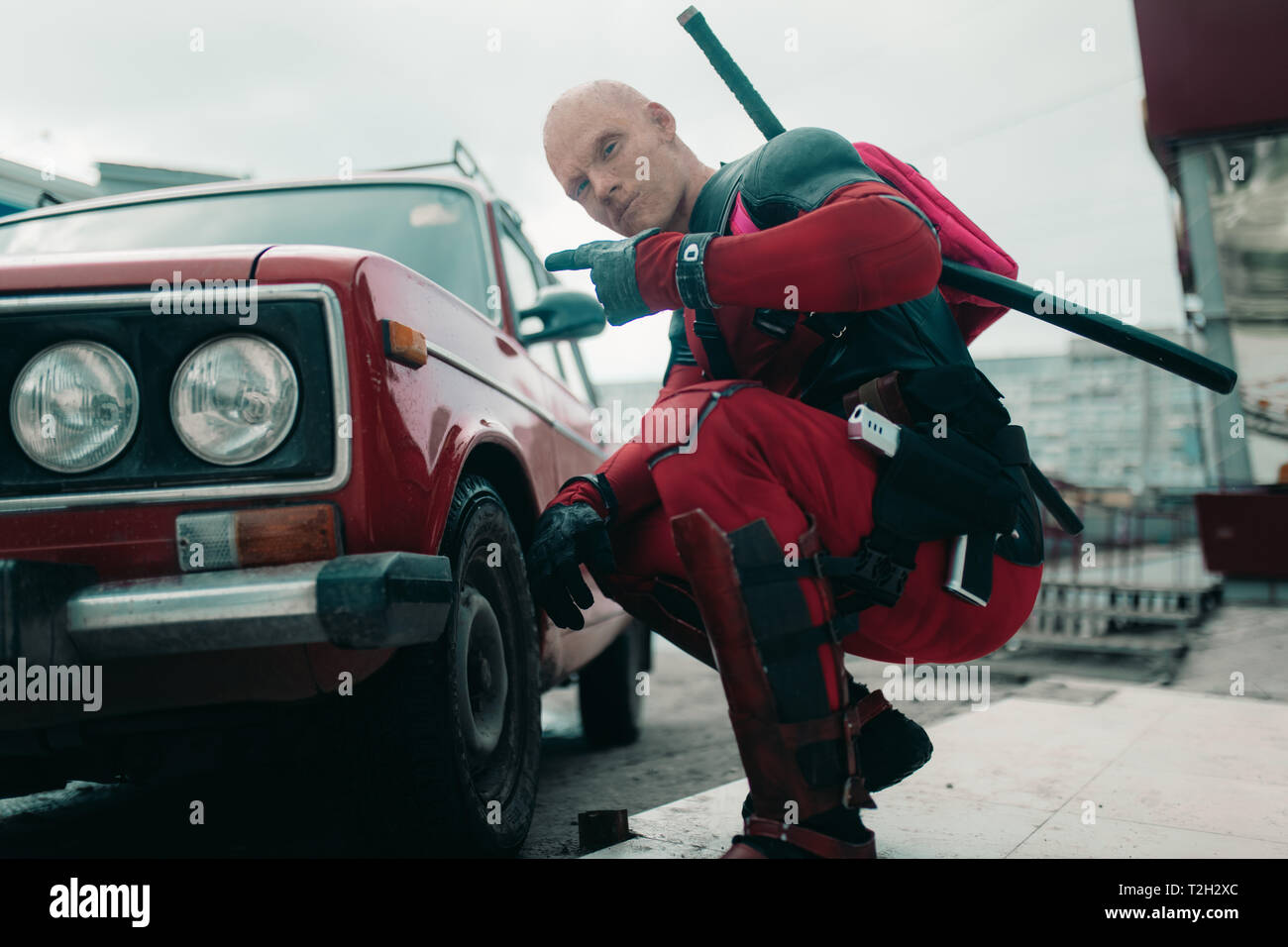 DNIPRO, UKRAINE - 28. MÄRZ 2019: Deadpool cosplayer mit Gewehr und katanas  hinter seinem Rücken neben der retro Auto posiert Stockfotografie - Alamy