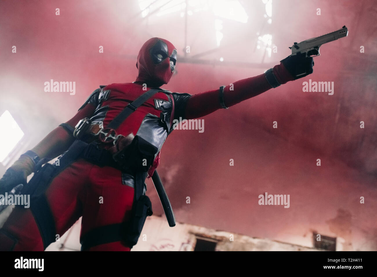DNIPRO, UKRAINE - 28. MÄRZ 2019: Deadpool cosplayer im Innenbereich mit zwei Pistolen in der Hand posiert auf dem Hintergrund von Rauch. Stockfoto