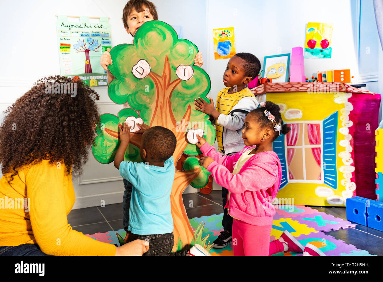 Gruppe von Kindern stellen Buchstaben des Alphabets auf dem Baum im Kindergarten Stockfoto