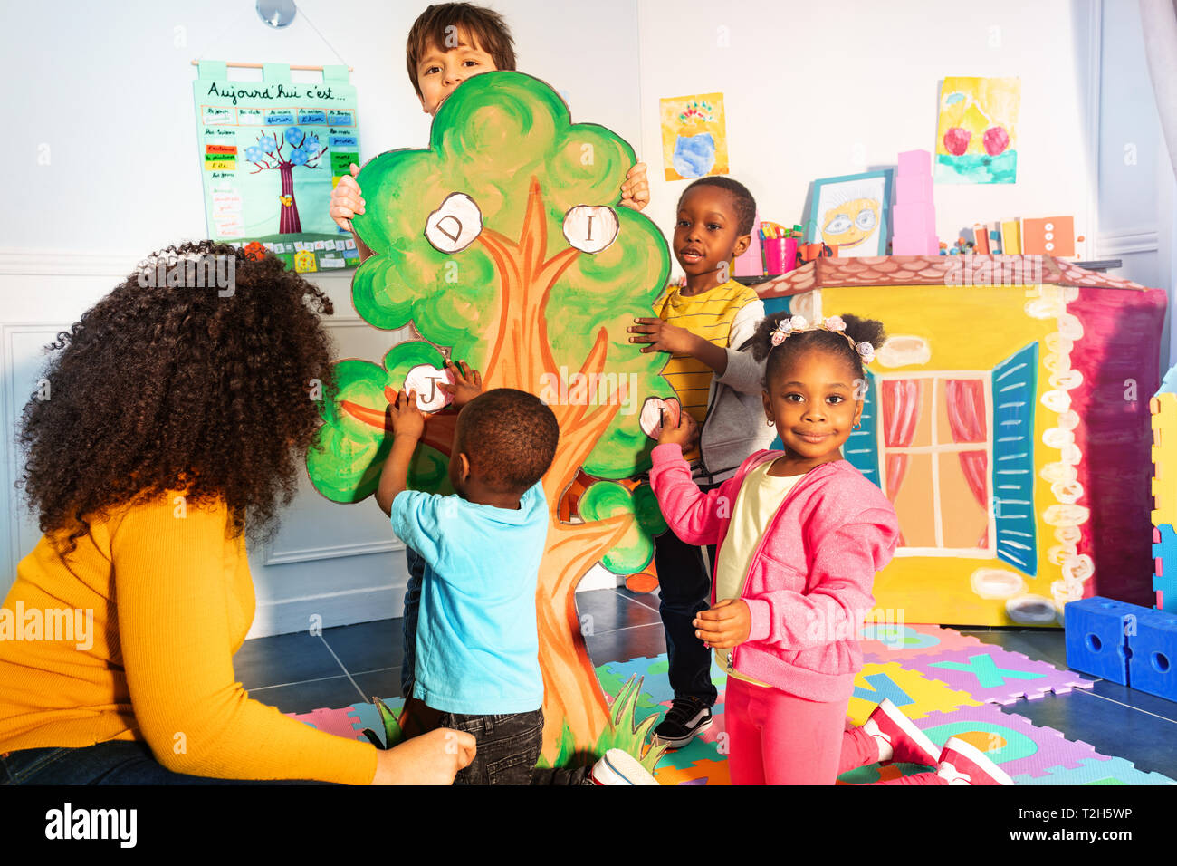 Kleine Kinder im Kindergarten Buchstaben auf den Baum wie Entwicklung Spiel mit Lehrer Stockfoto