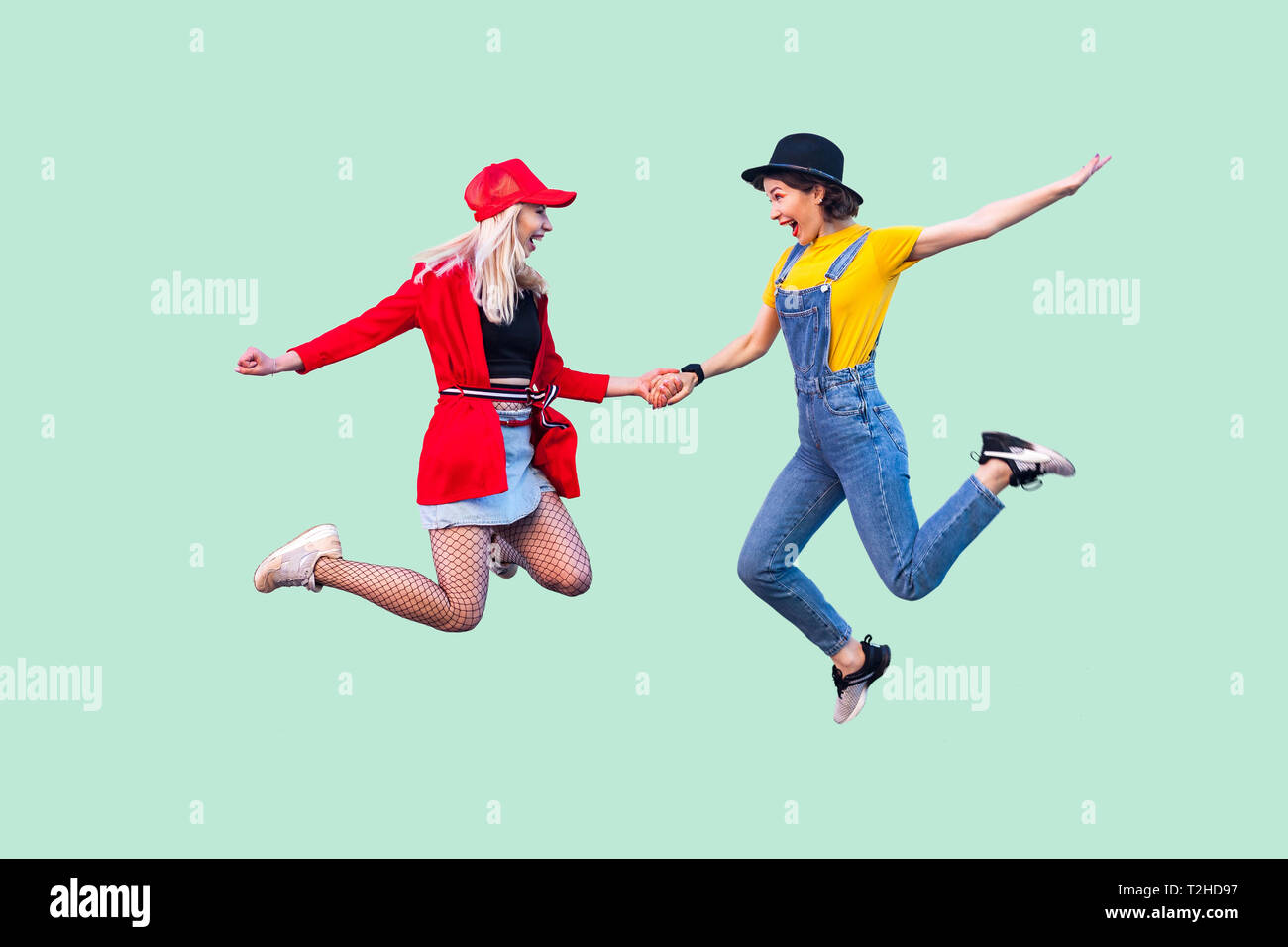 Volle Beine Körper größe Portrait von zwei glückliche Schreien stilvolle hipster Mädchen in modische Kleidung springen in die Luft und feierte einen Gewinn. Pflege Stockfoto
