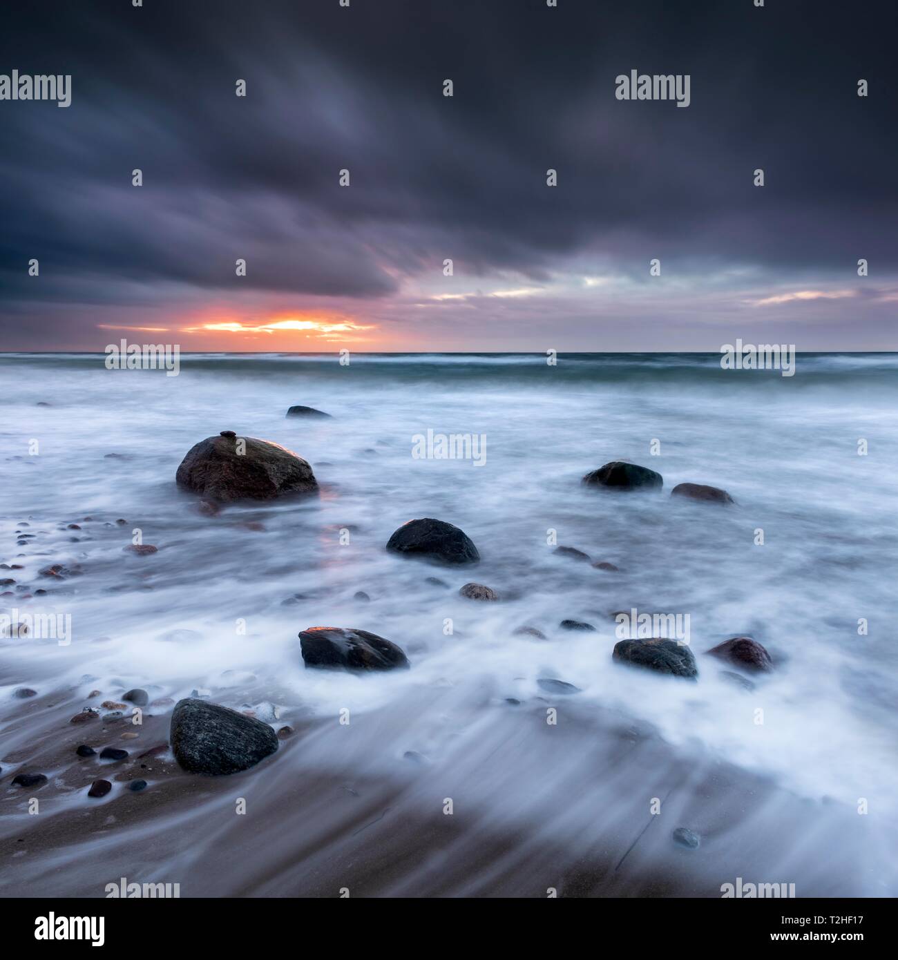 Stürmische See mit dunklen Wolken bei Sonnenuntergang am Strand der Ostsee, Felsen in der Brandung, Halbinsel Fischland-Darß-Zingst, Mecklenburg-Vorpommern Stockfoto