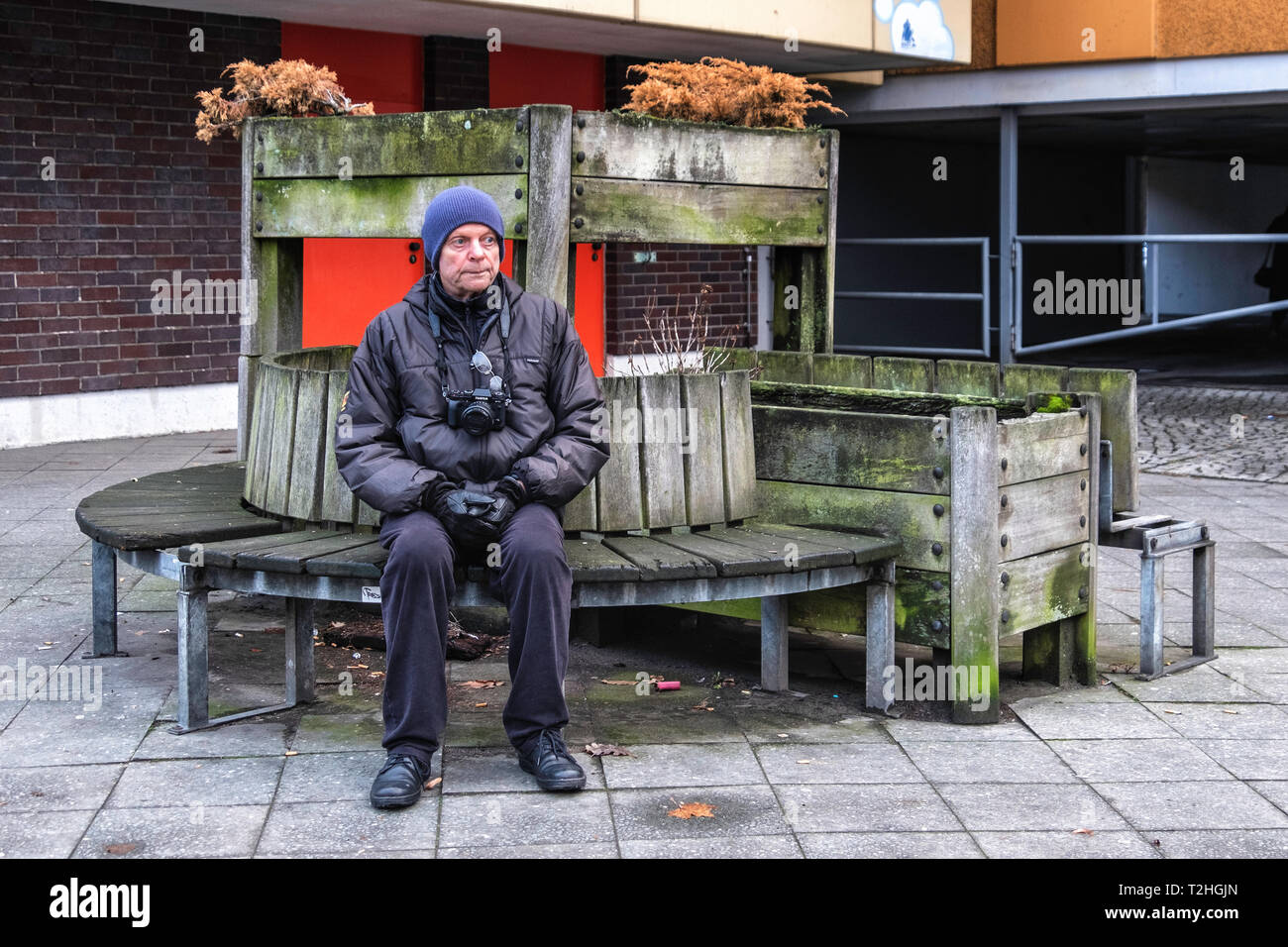 Älterer Mann mit Kamera beruht auf einer Bank in Moabit, Berlin. Rustikale Holzbank mit Blumentöpfe Stockfoto