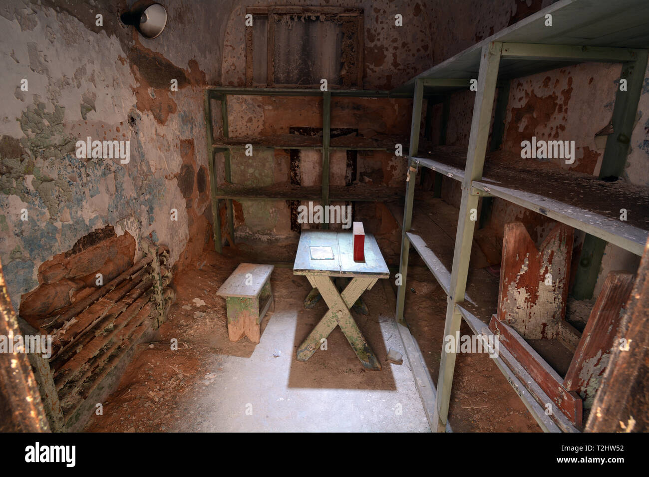 Östliches Staatszuchthaus - Zelle mit Fachböden aus Holz, Tisch und Stuhl, in einem verlassenen Gefängniszelle Stockfoto