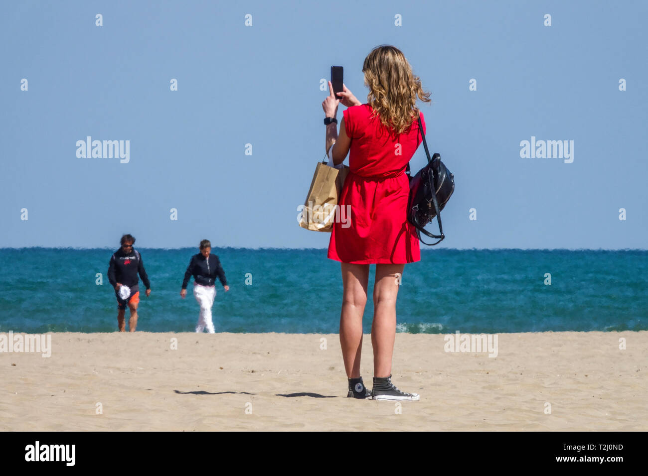 Valencia Strand Malvarrosa, eine junge Frau in rotem Anzug machen ein Foto auf mobile, Rückansicht Spanien Meerblick Valencia Strandurlauber Stockfoto