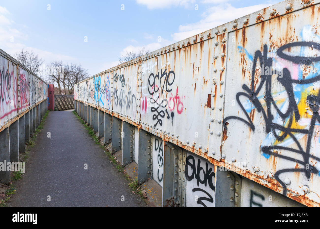 Sprühfarbe grafitti auf ein altes rostiges Eisen bahn Brücke auf einem Fußweg in Woking, Surrey, England, Großbritannien Stockfoto