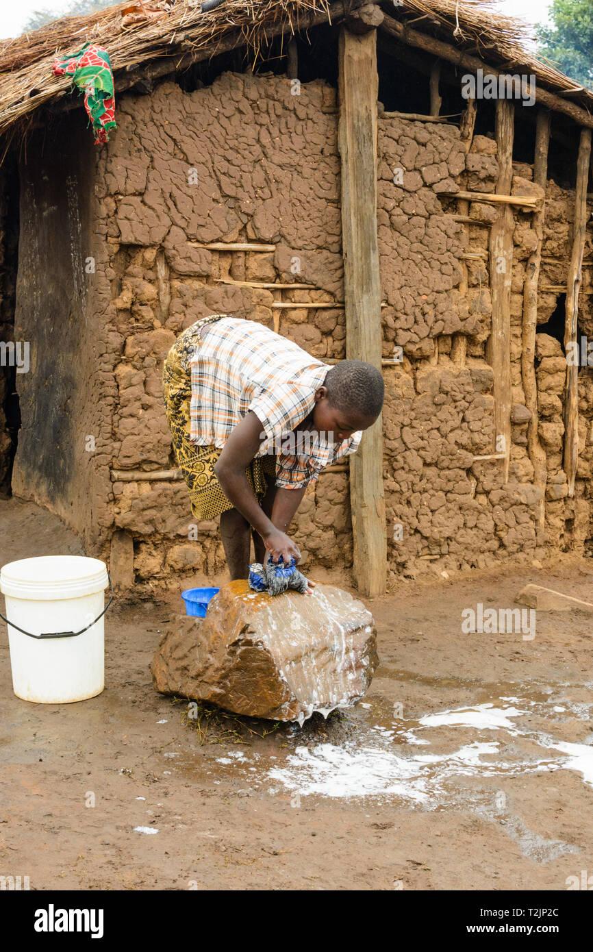 Malawische Mädchen wäscht Kleidung auf einem Stein vor einer Lehmhütte in einem Dorf Stockfoto