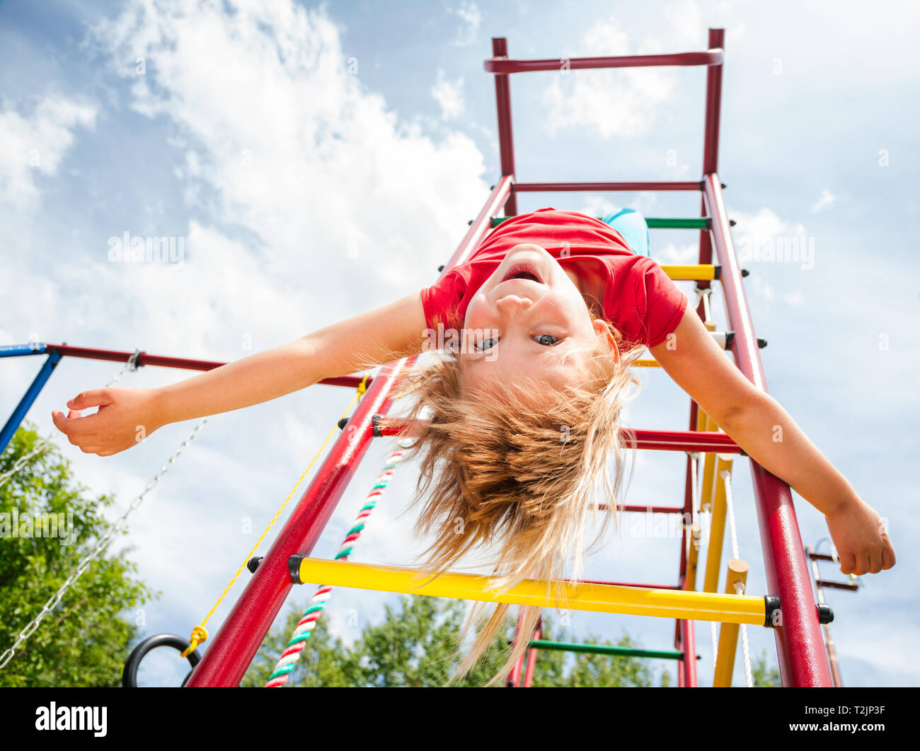 Elementare alter Mädchen hing kopfüber von einem Jungle Gym (Monkey Bars oder klettergerüst) auf einem Spielplatz im Sommer genießen. Stockfoto