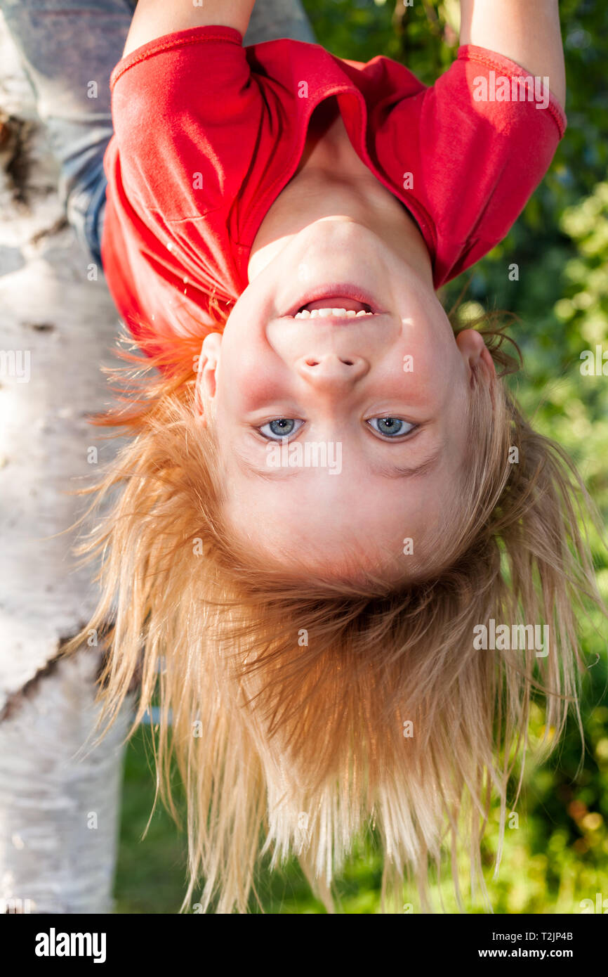Portrait von Happy elementare Alter Mädchen tragen rote T-Shirt kopfüber von einem Ast hängen - Sommer Spaß Konzept Stockfoto