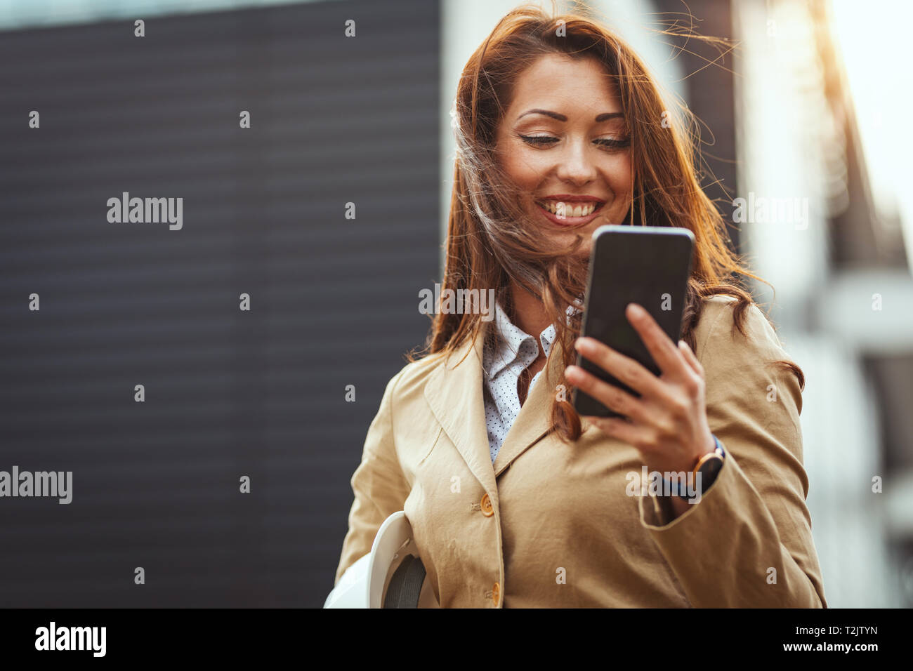 Schöne junge Frau Überprüfung der Nachricht auf Ihrem Smartphone unterwegs gegen Stadt Hintergrund. Stockfoto