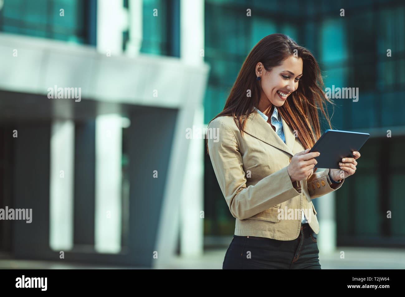 Schöne junge erfolgreiche lächelnde Frau Überprüfung der Nachricht auf Ihrem Smartphone unterwegs gegen Stadt Hintergrund. Stockfoto