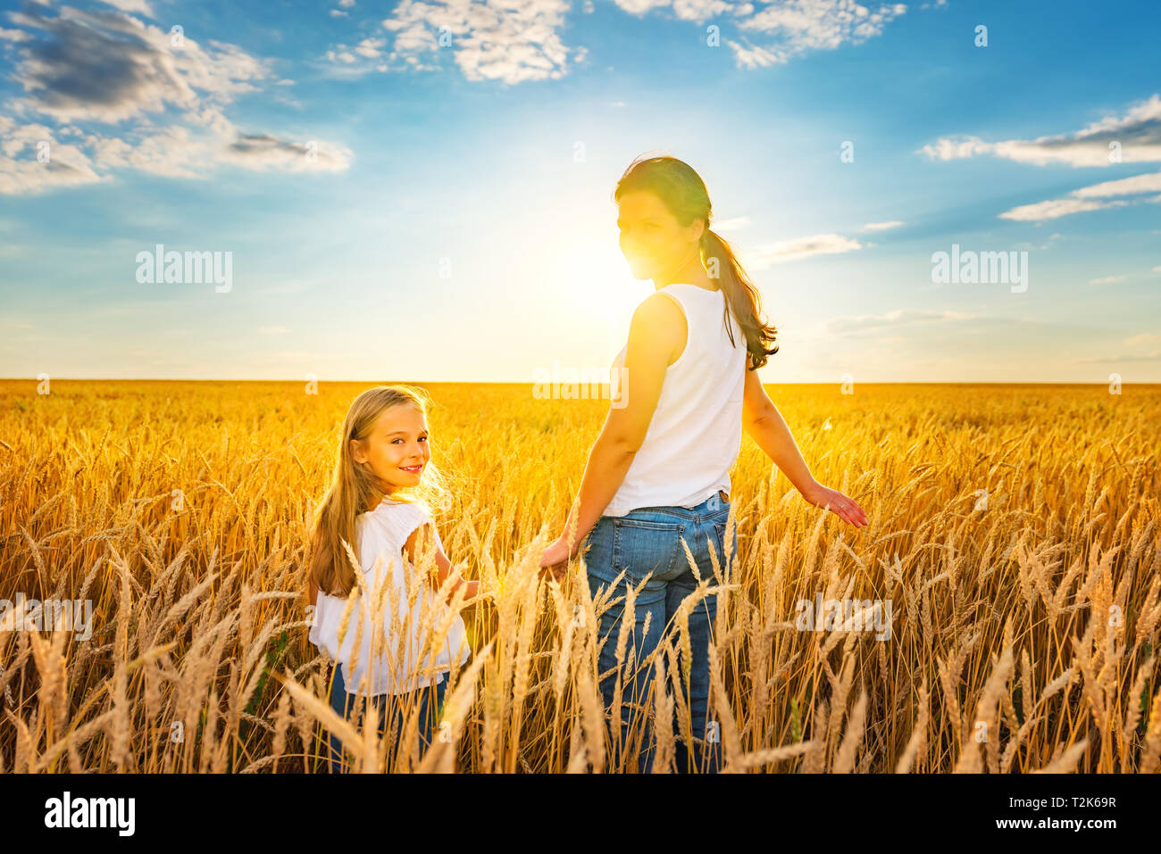 Junge Frau und ihre Tochter zu Fuß auf goldenen Weizenfeld am sonnigen Sommerabend. Stockfoto