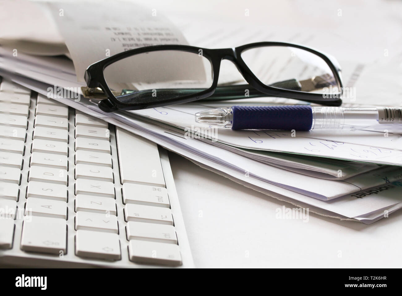 Computer Tastatur, Brille, Bleistift und unordentliche Papiere liegen auf einem weißen Tisch Stockfoto