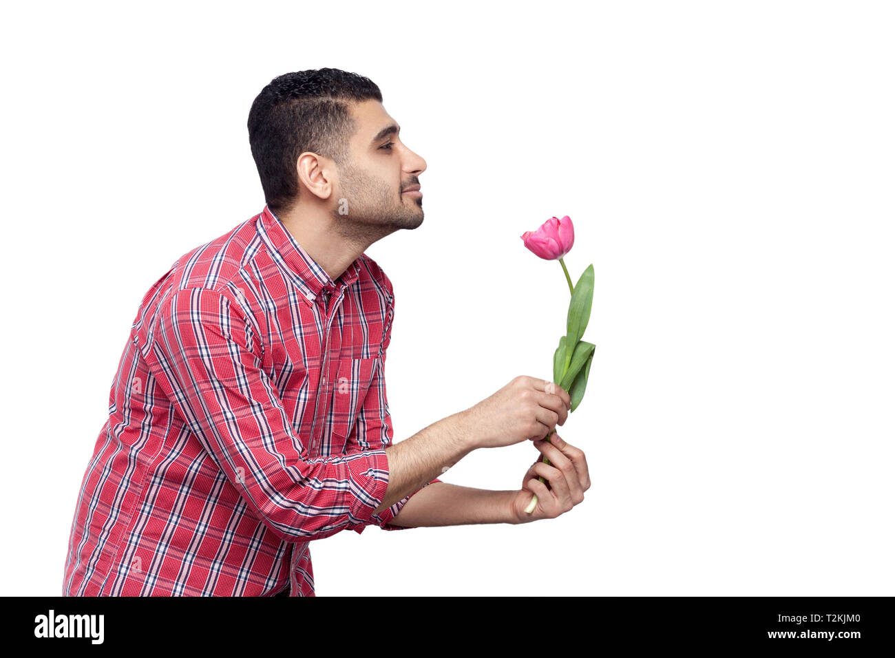 Seite Profil ansehen Portrait von Stattlichen bärtiger junger Mann in rot kariertem Hemd und eine Tulpe Blume Holding und lächelnd und gerade auf der Suche Stockfoto