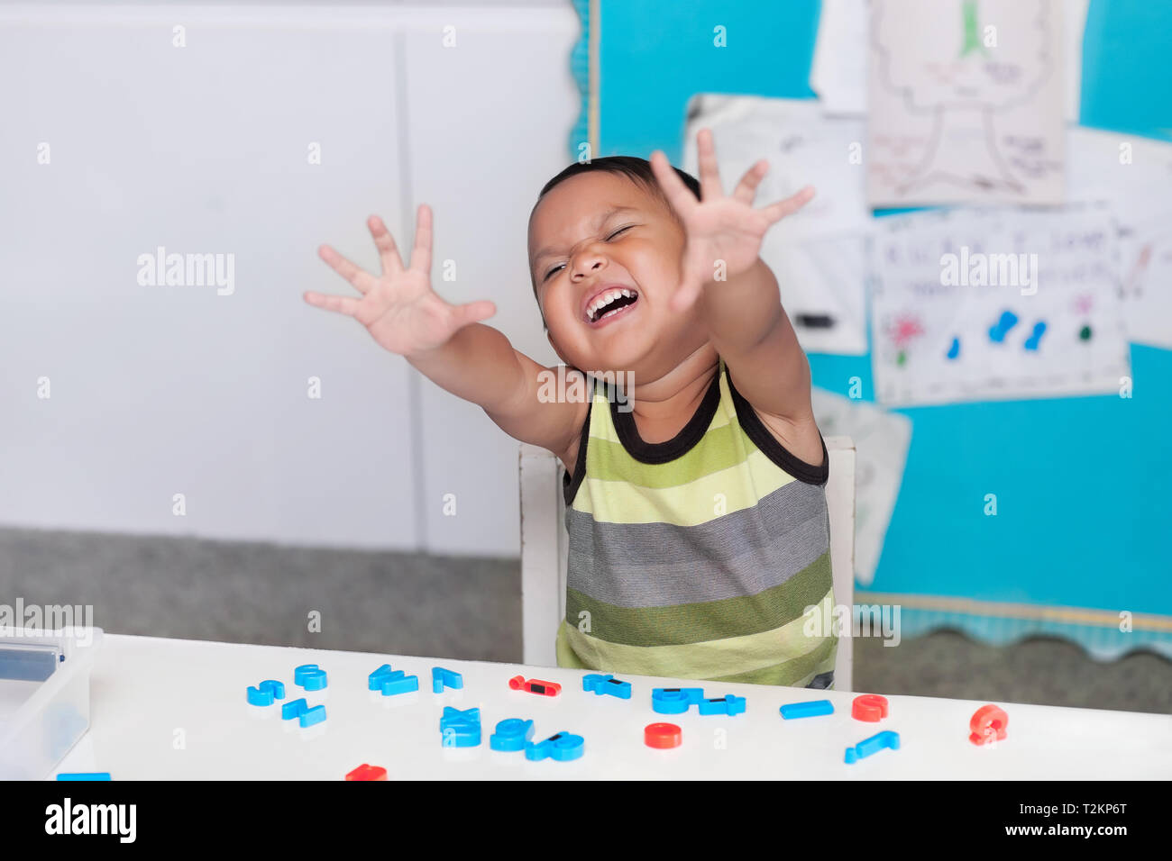 Hispanic junge Ausdruck störend oder ordnungswidriges Verhalten in ein Klassenzimmer mit Buchstaben manipulatives auf dem Schreibtisch. Stockfoto