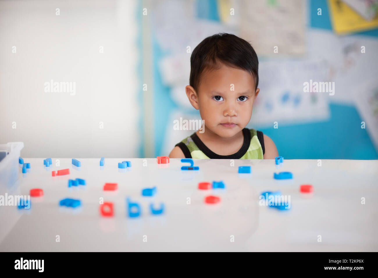 Junge Schwierigkeiten beim Lernen in einem Kindergarten mit Buchstaben des Alphabets auf dem Schreibtisch. Stockfoto